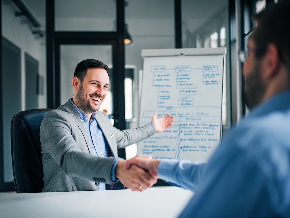 Smiling millennial businessman handshaking coworker, celebrating successful teamwork.